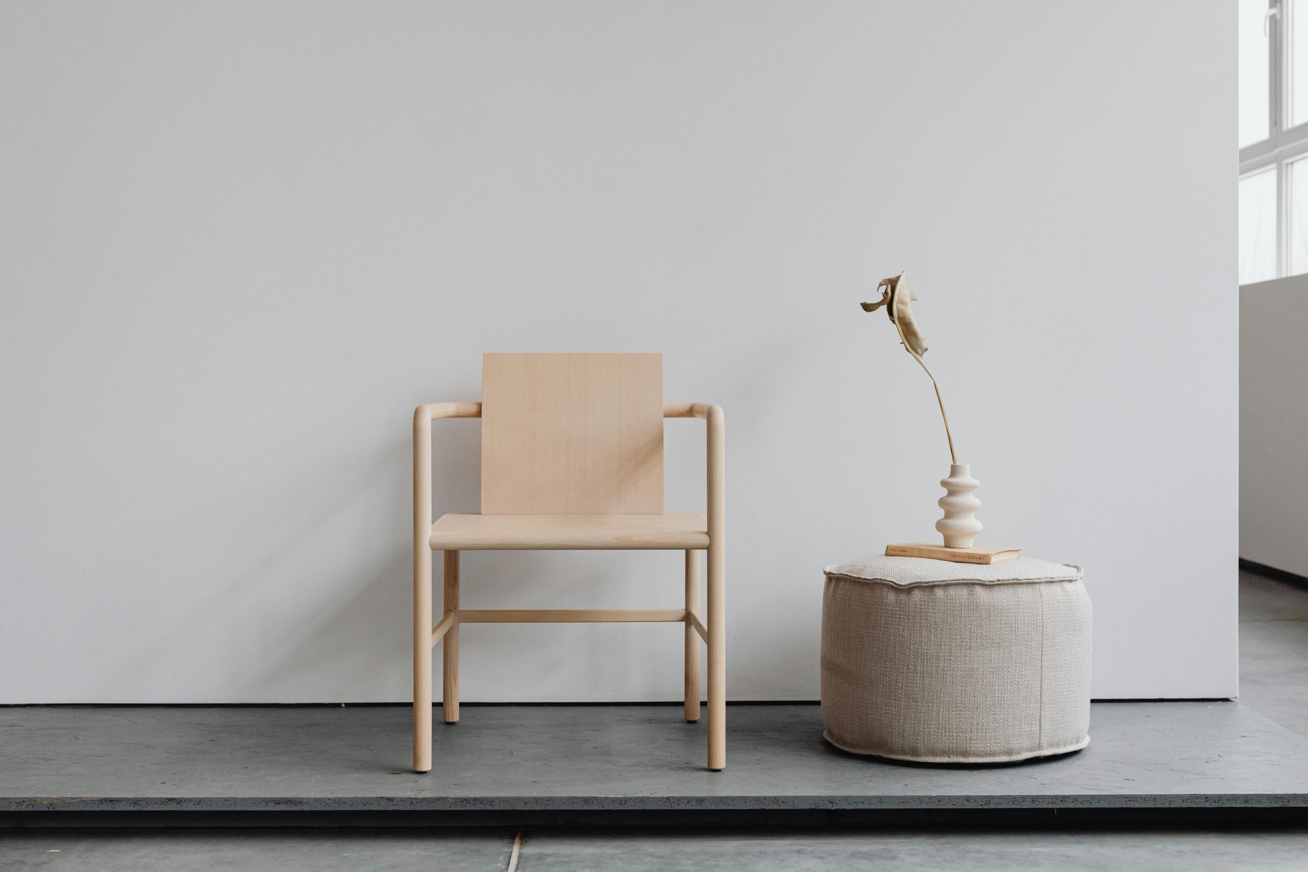 Simple yet elegant minimalist furniture featuring a wooden chair and pouf in a bright modern interior.